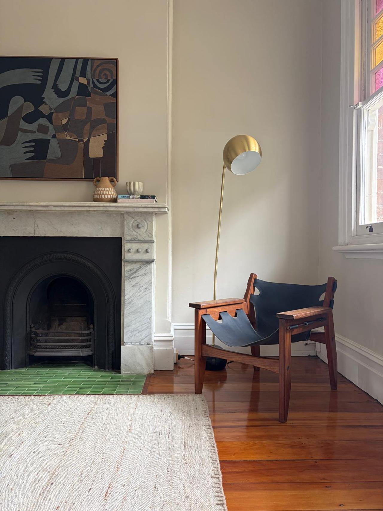 Marble fireplace with a green tiled hearth, dark leather sling chair and brass arc floor lamp beside a stained-glass window