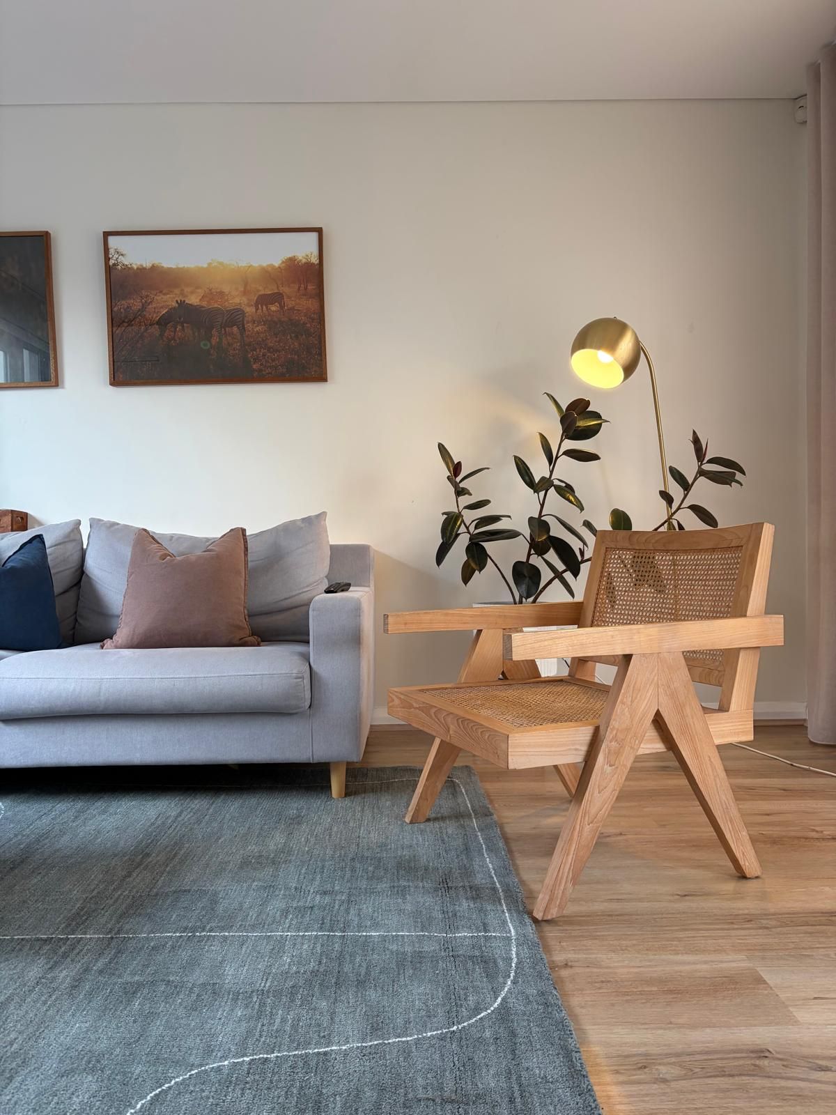 Living room with a grey sofa, brass arc floor lamp and rattan-and-timber armchair beneath a zebra photograph print