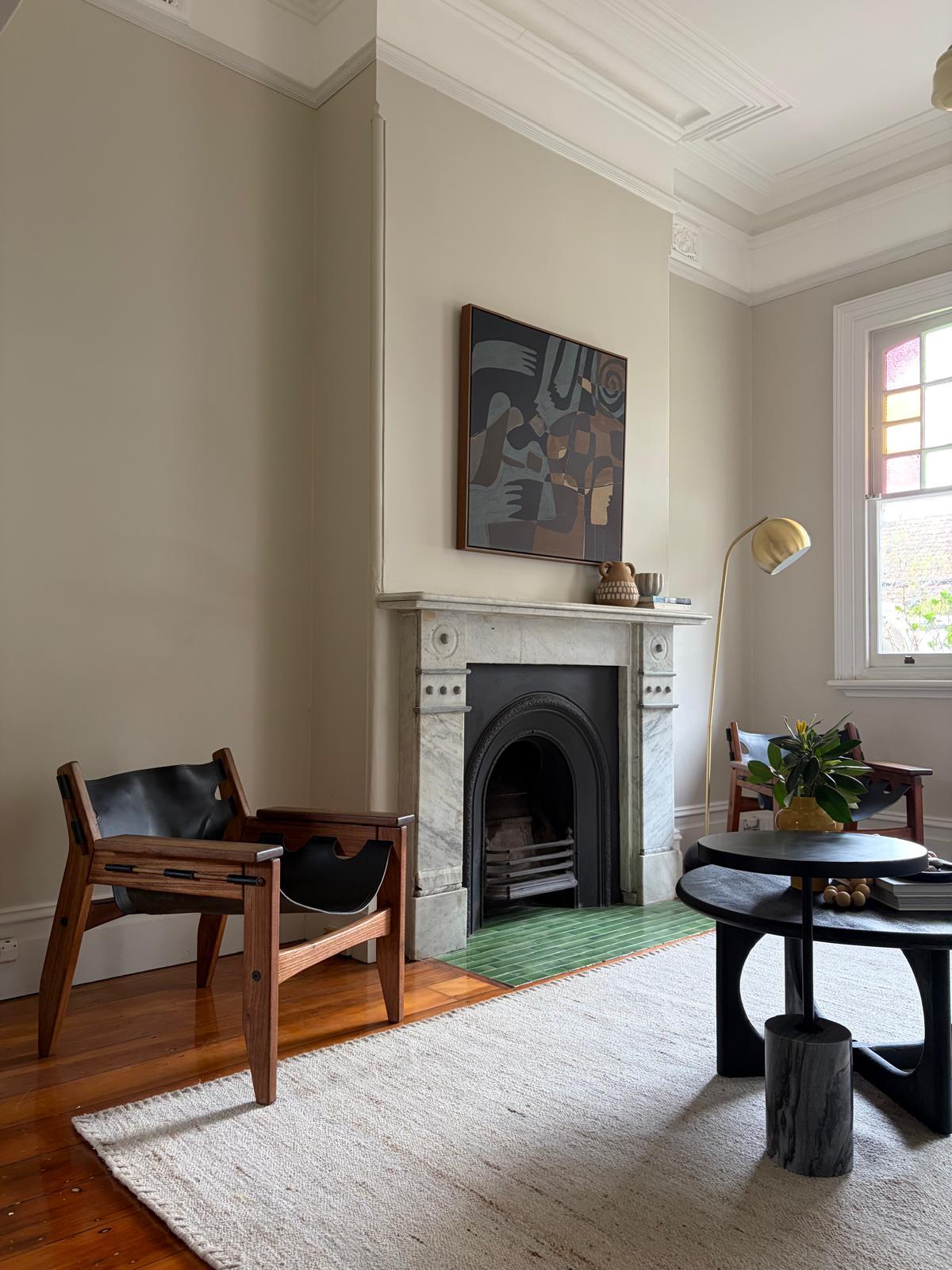 Living room fireplace with a round black side table and timber chair beside the marble mantel