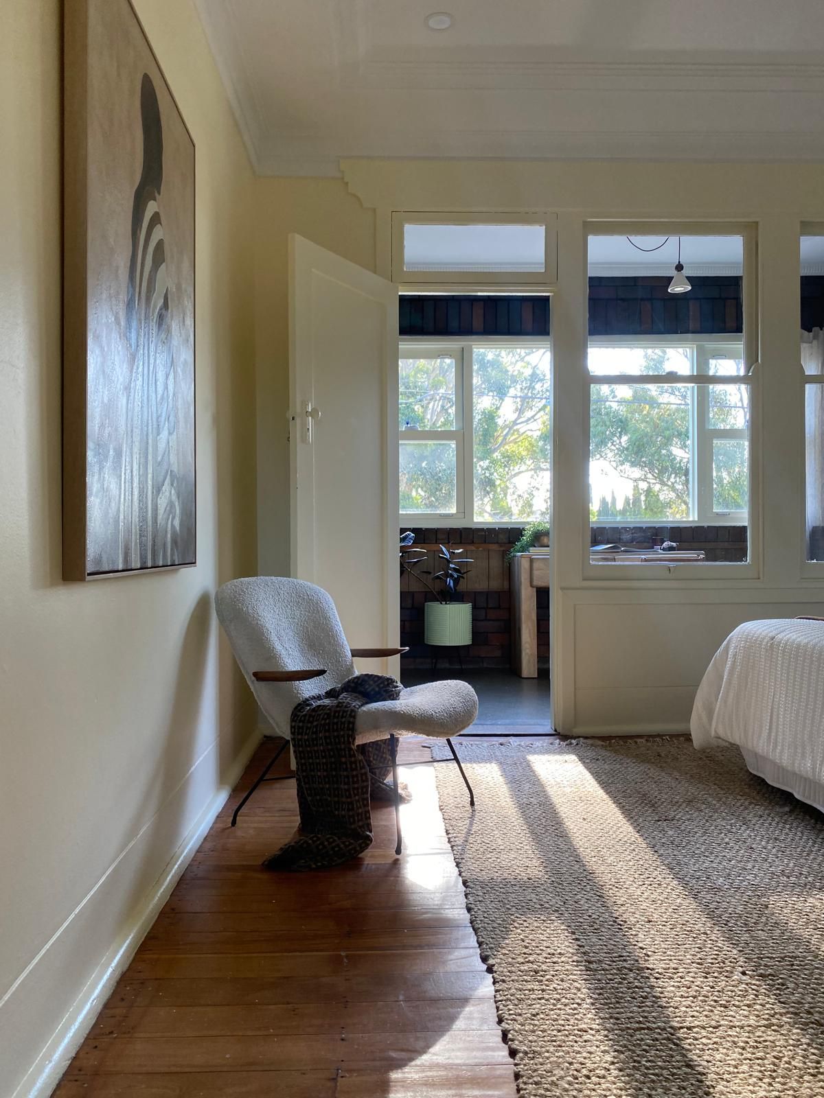 Sunlit bedroom corner with a boucle armchair and throw blanket, opening onto a sunroom