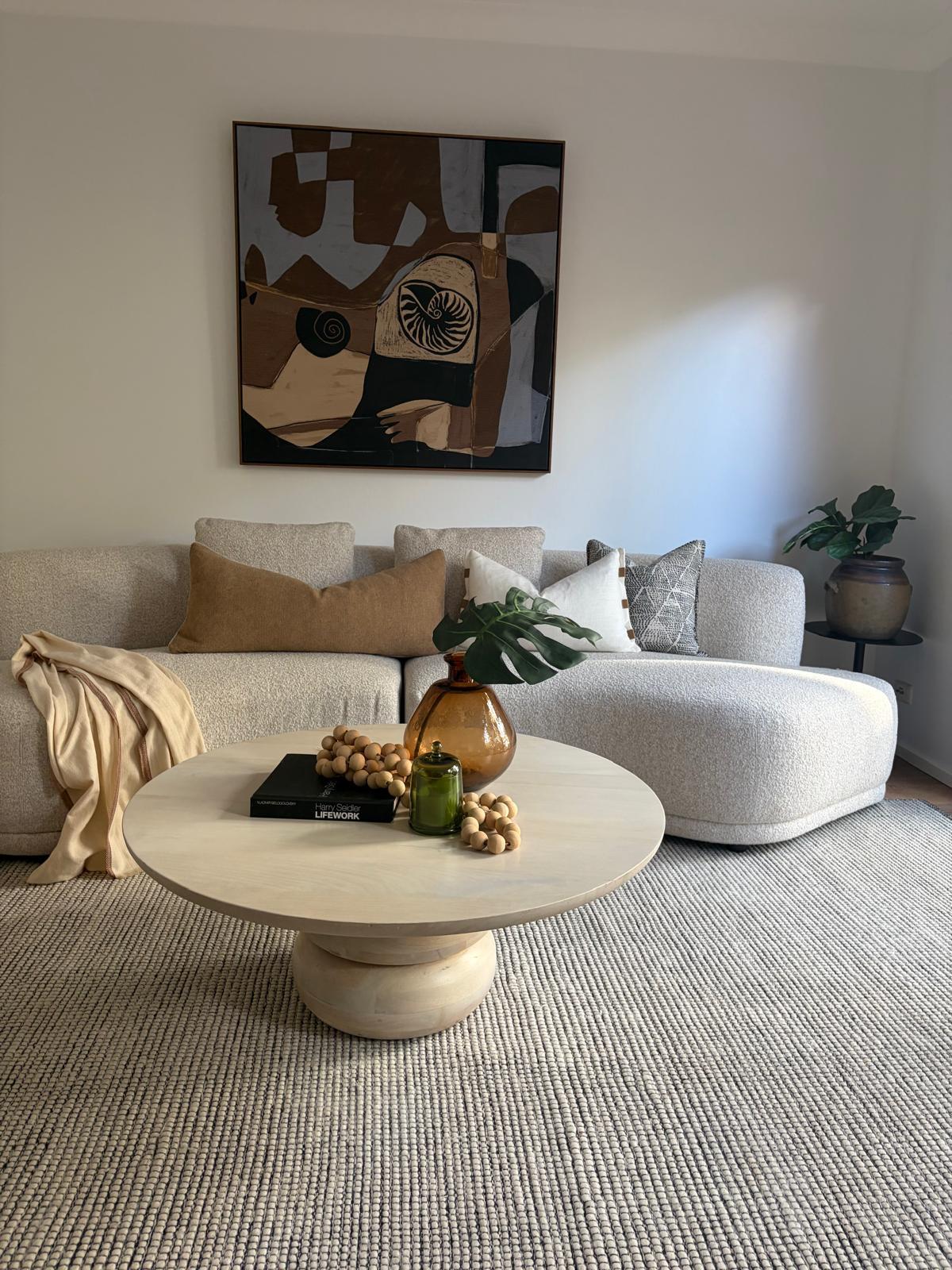 Neutral lounge with a channel-tufted boucle sofa and dark curved armchair, under an ornate pressed-metal ceiling