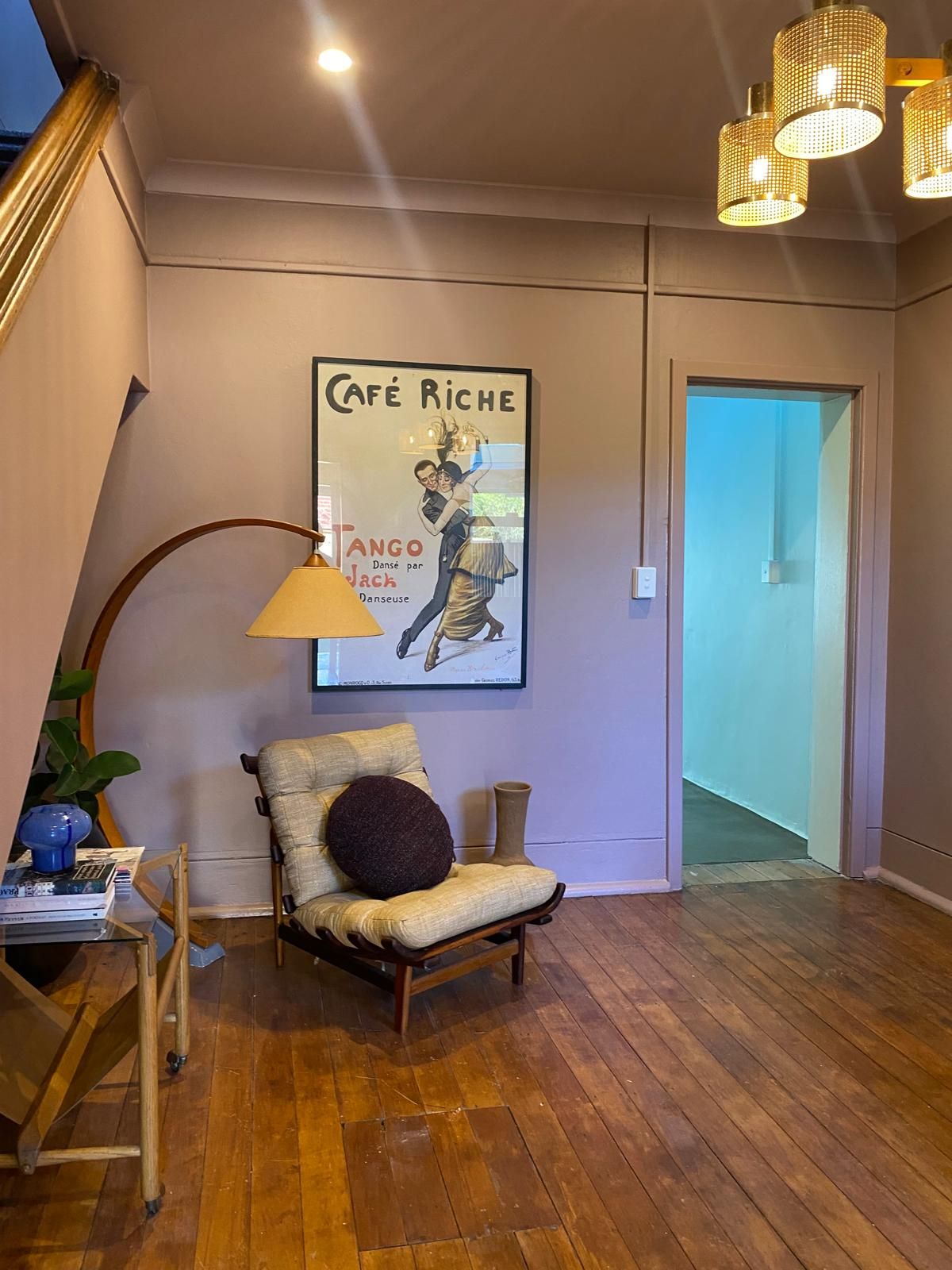 Mauve-toned living room with a vintage Cafe Riche tango poster, mid-century lounge chair and an arched timber floor lamp
