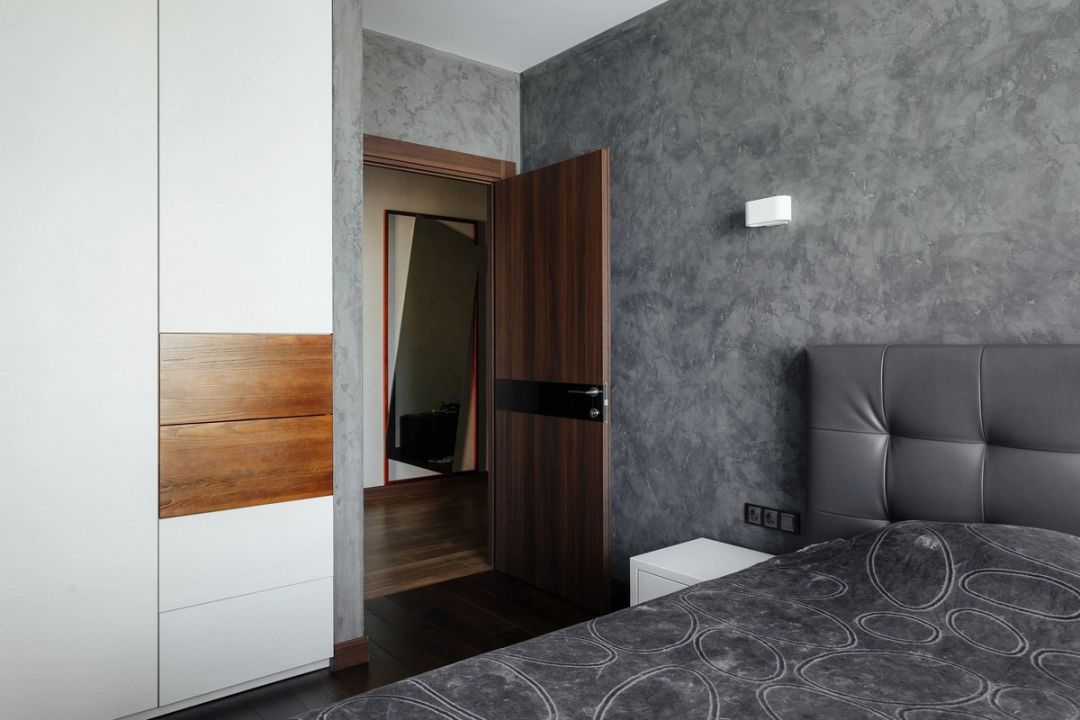 Camera da letto con testiera capitonné grigia, pareti in stucco materico e armadio bianco con inserti in noce