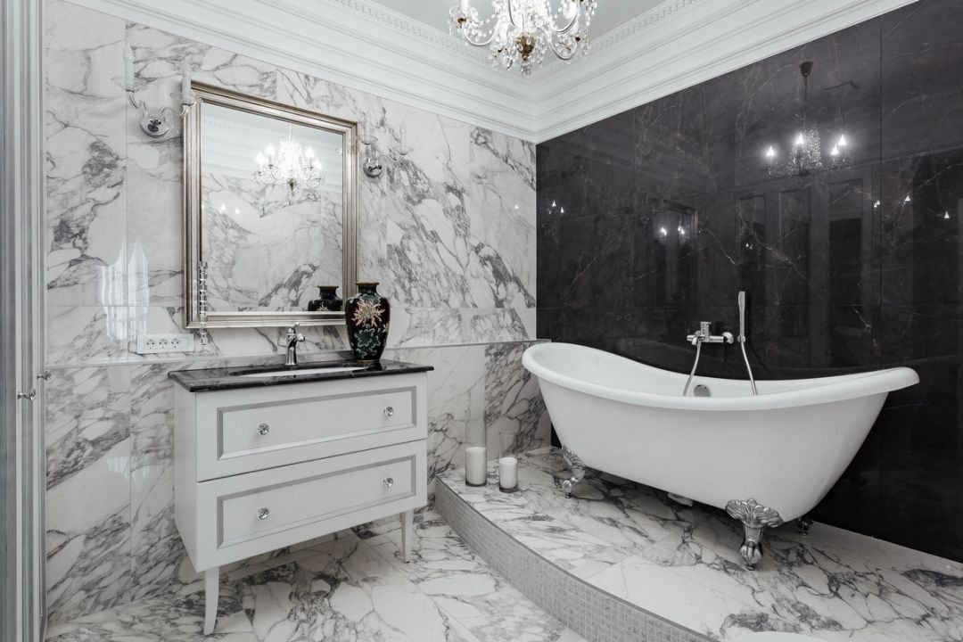 Bagno padronale in marmo arabescato, con vasca su piedini cromati e parete di fondo in marmo nero