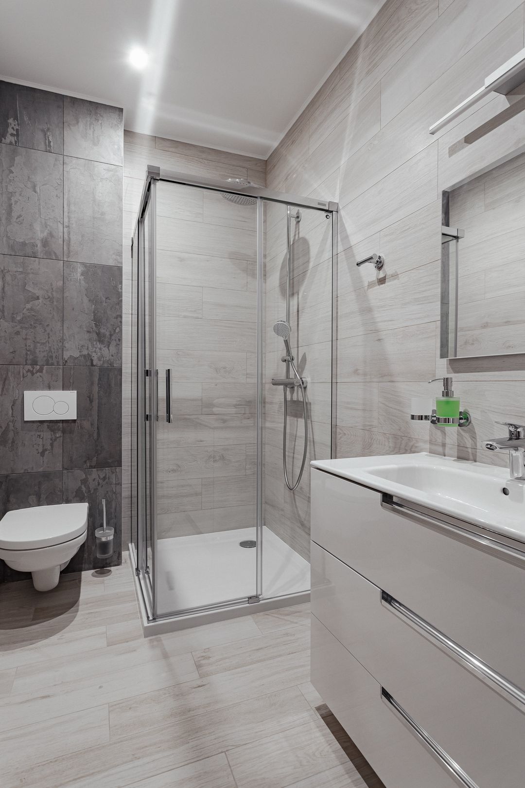 Bagno con gres effetto legno chiaro, parete in ardesia scura e box doccia in cristallo.
