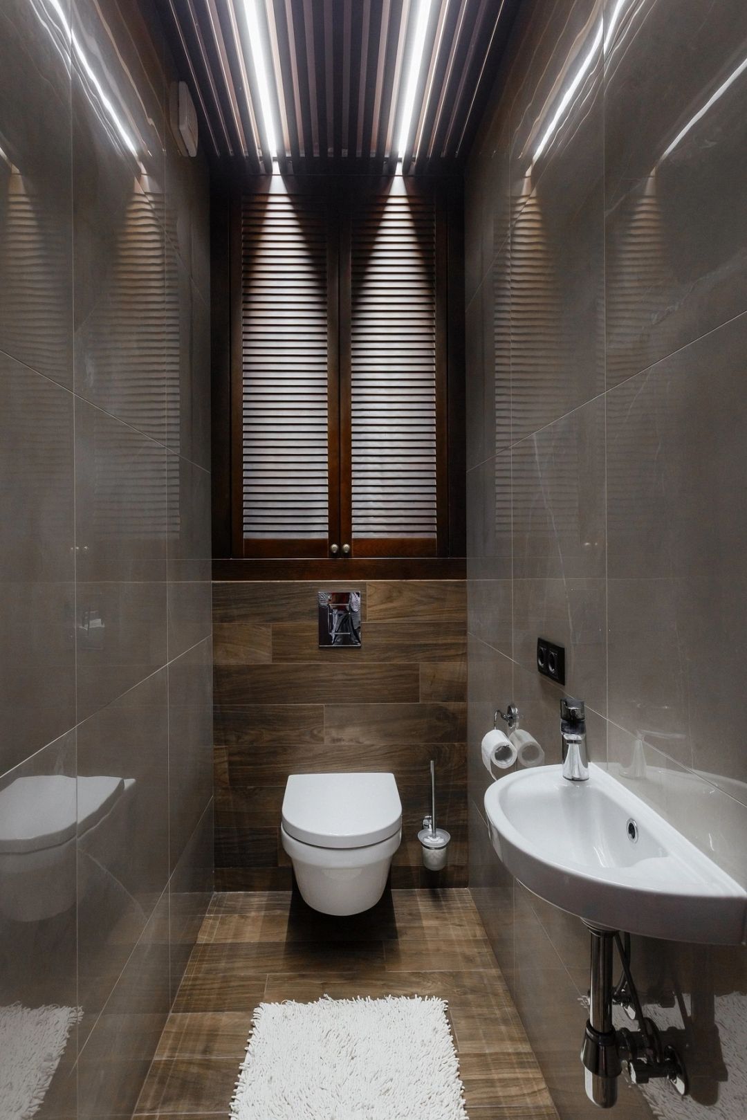 Bagno di servizio in gres effetto marmo e legno, con controsoffitto a doghe e anta a persiana