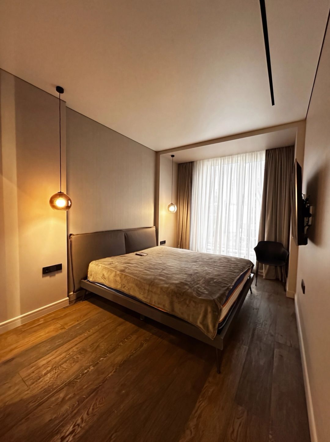Camera da letto dalla calda luce serale, con pavimento in legno e tende a tutta altezza