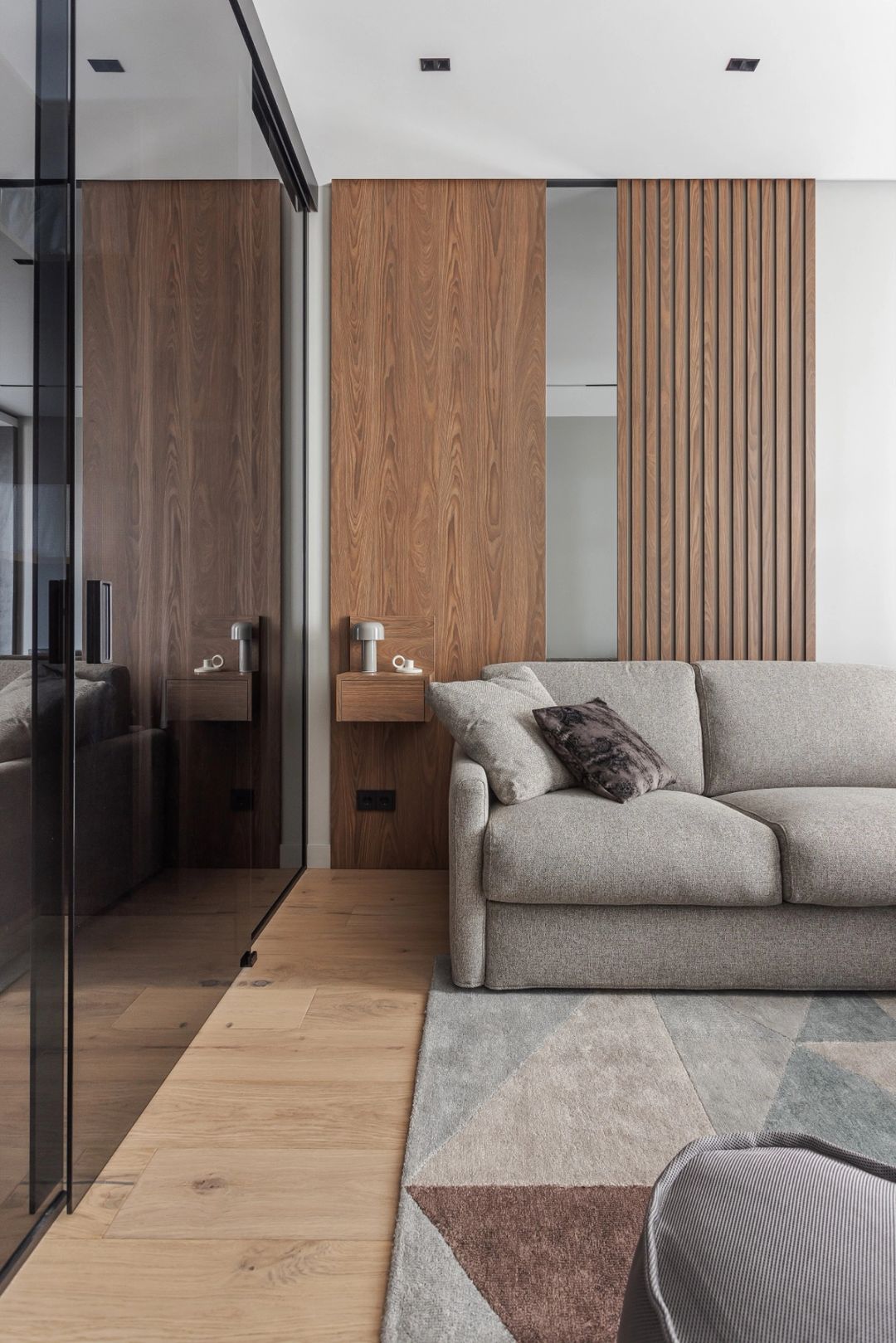 Zona relax con divano grigio, parete in boiserie di legno e partizione in vetro