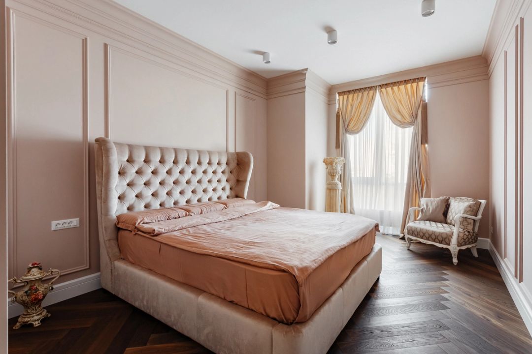 Camera da letto in rosa cipria, con testiera capitonné, parquet a spina di pesce e tende dorate