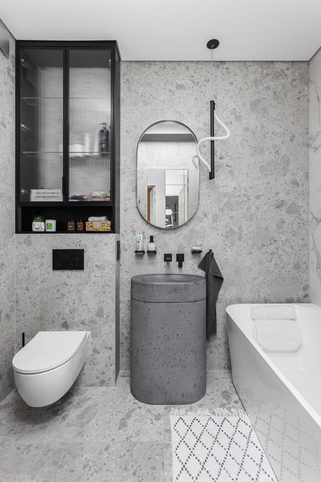 Bagno in terrazzo grigio, con specchio ovale e lavabo in cemento