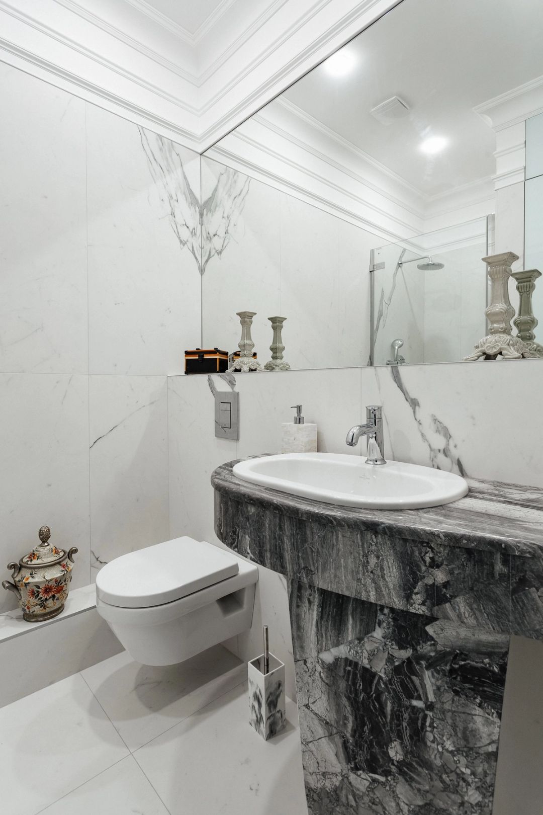 Secondo bagno rivestito in marmo bianco, con lavabo monolitico in marmo grigio e specchio a tutta parete