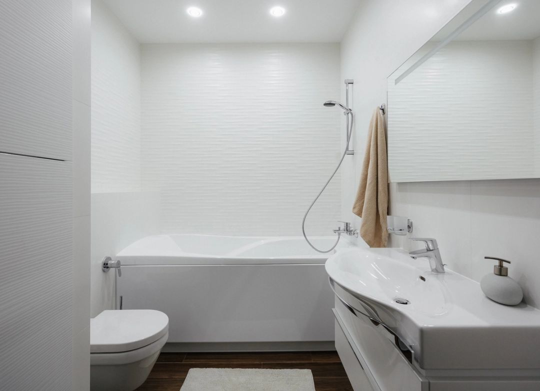 Bagno padronale in ceramica bianca a rilievo ondulato, con vasca, lavabo sospeso e pavimento scuro