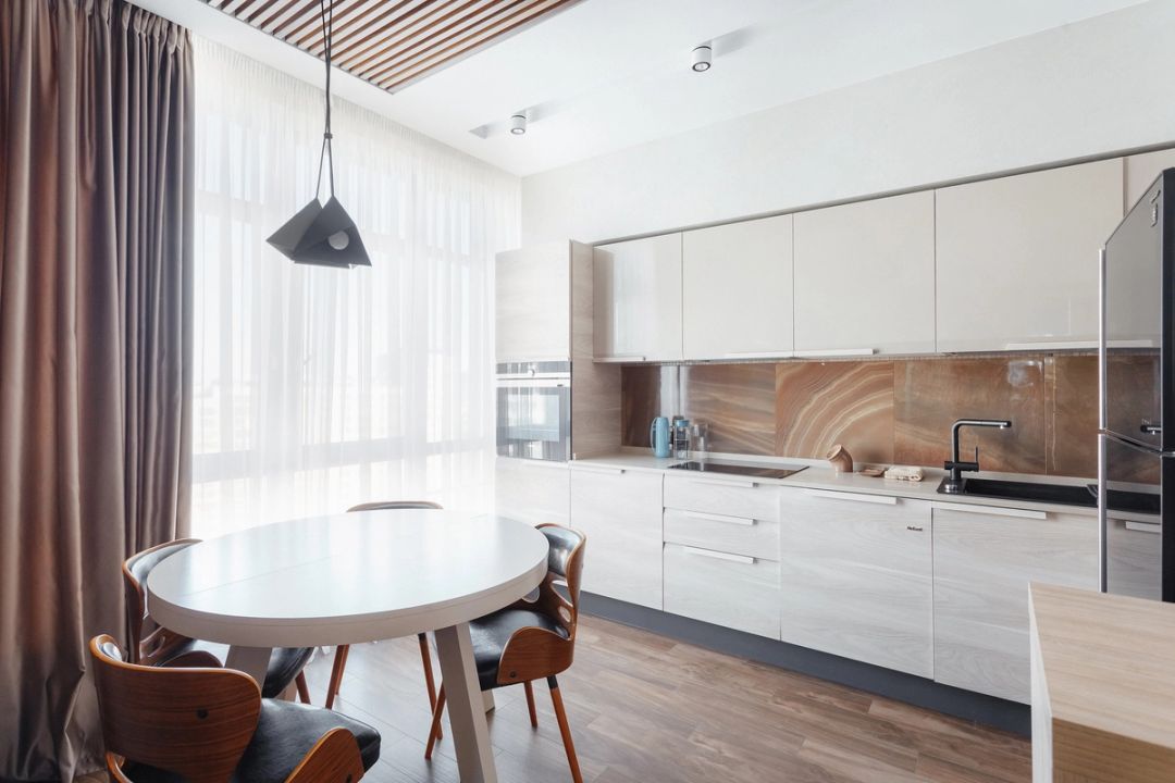 Cucina lineare beige con paraschizzi in onice, tavolo tondo bianco e soffitto a doghe di legno