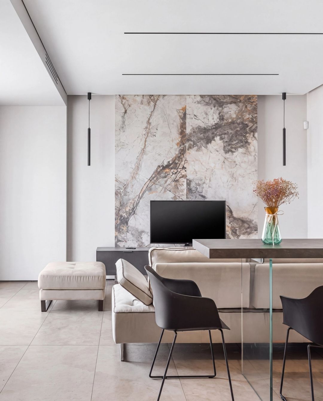 Zona giorno con una scenografica parete in pietra effetto marmo, divano beige e sedute nere