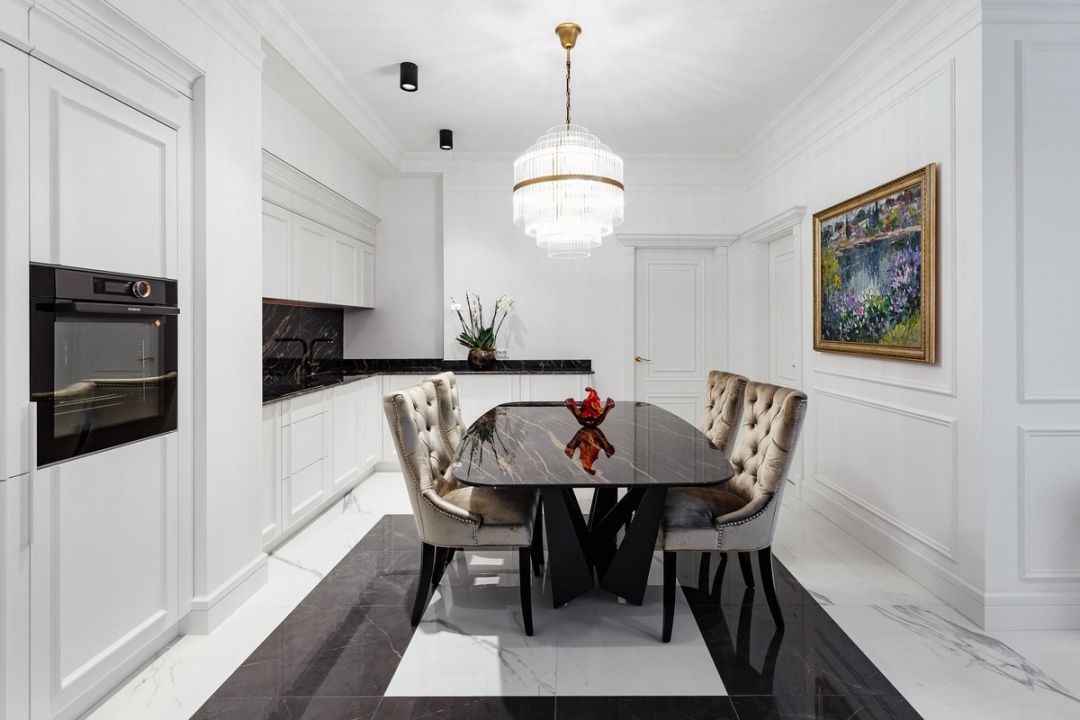 Cucina-sala da pranzo in bianco laccato, con top e tavolo in marmo nero e lampadario in cristallo e ottone