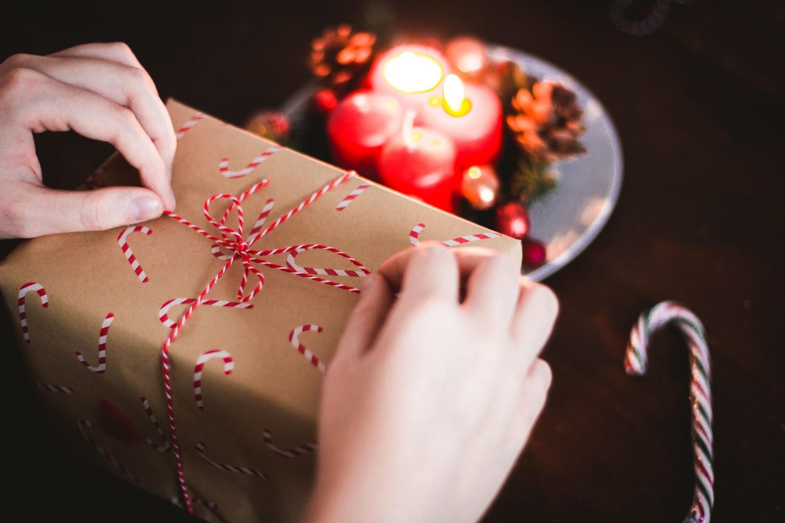 WhatsApp Business: Manos abriendo un regalo navideño con una vela detrás