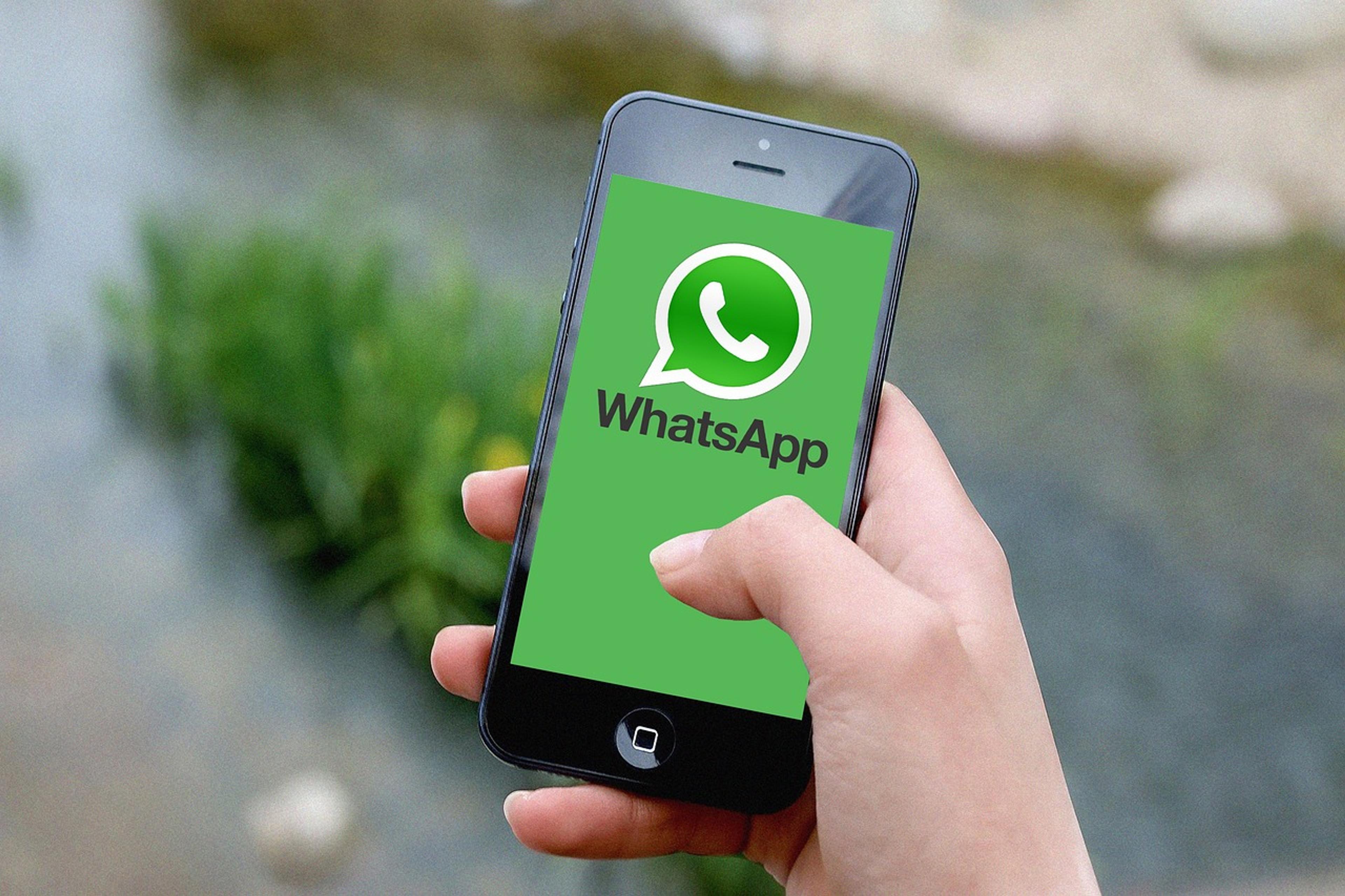 Una mano sosteniendo un celular con el logo de WhatsApp en la pantalla