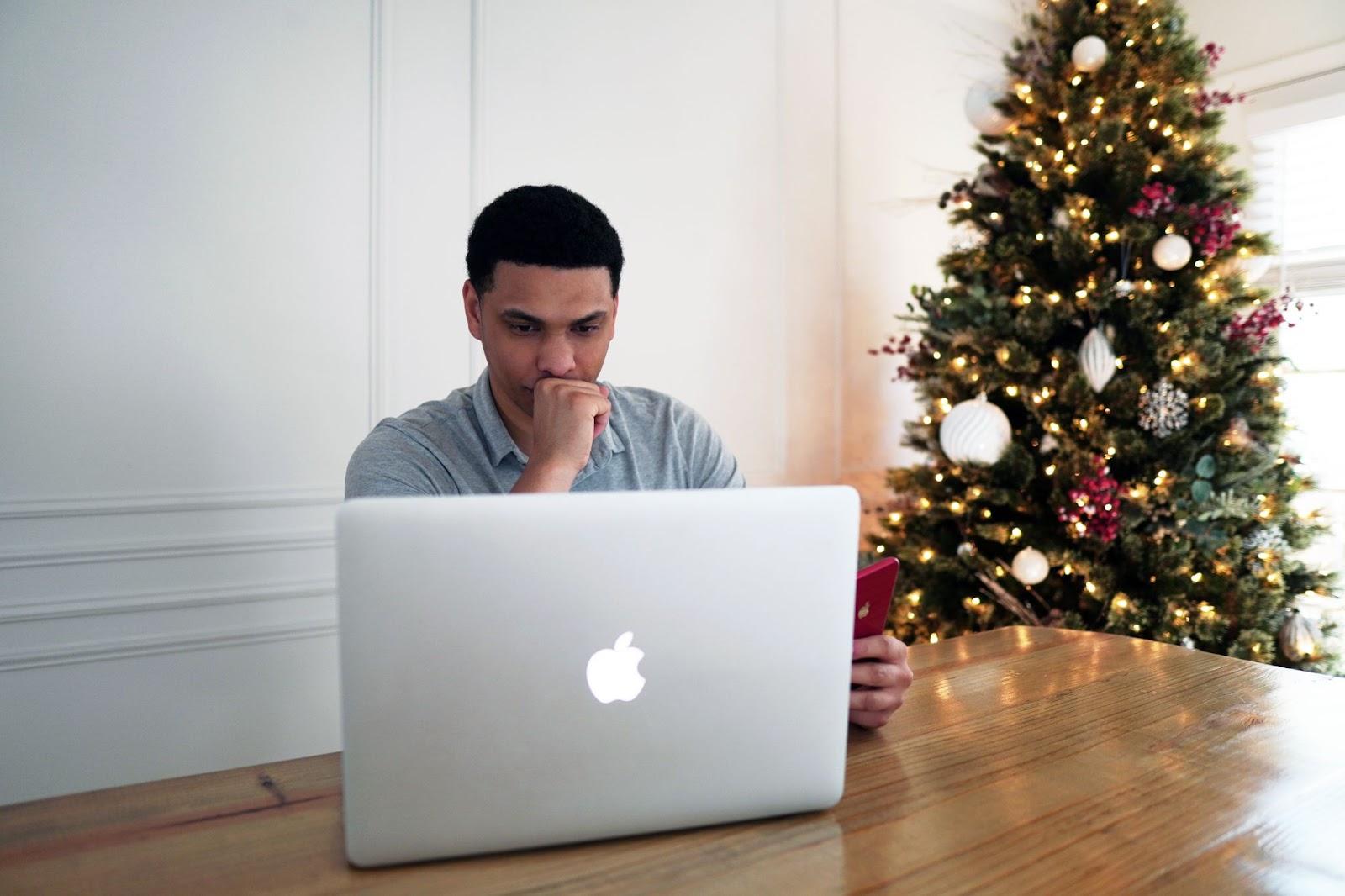 Hombre mirando un computadora con un árbol de navidad detrás. WhatsApp Business