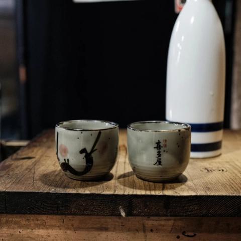 Dos vasos de cerámica y una botella de sake sobre una barra de madera