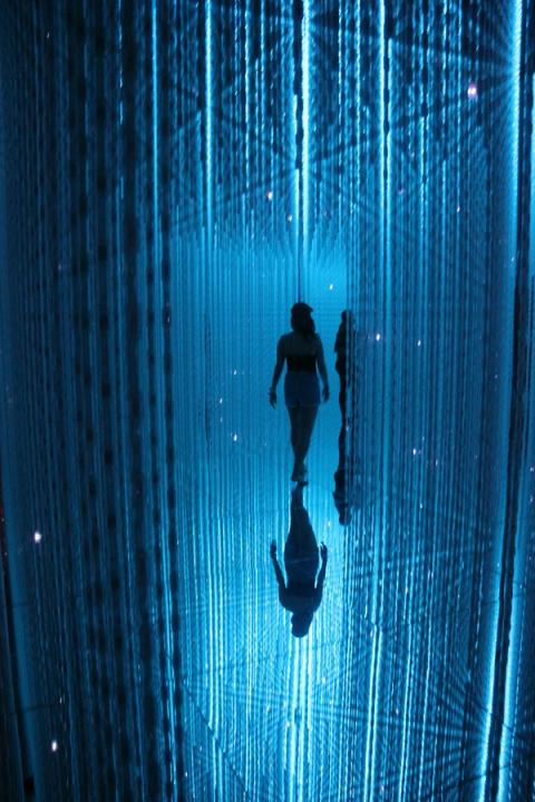 Una figura entre columnas de luz azul en una sala de arte digital