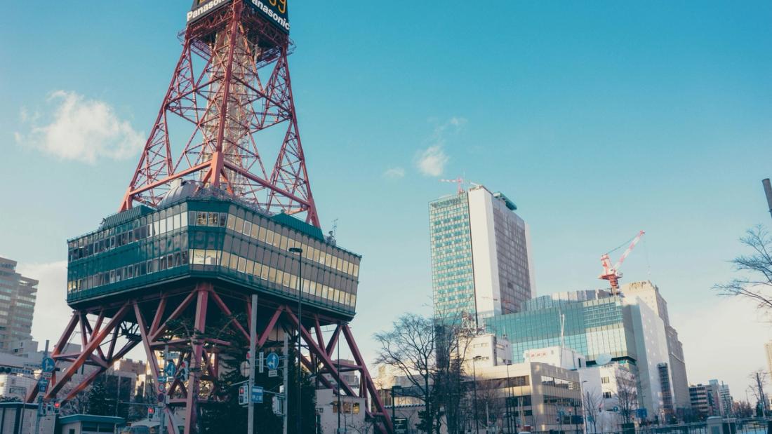 Torre de acero roja con plataforma de observación y letrero Panasonic en un parque urbano soleado