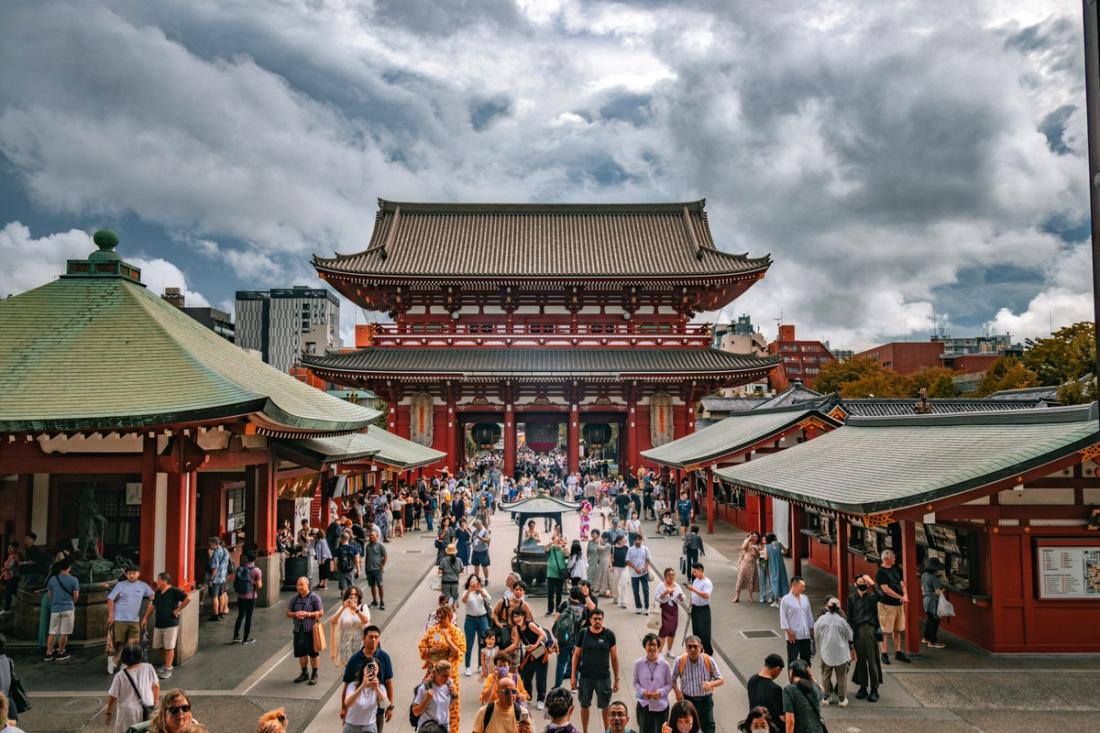 Multitud de visitantes en el patio de entrada de un gran templo budista rojo con tejados verdes bajo un cielo nublado