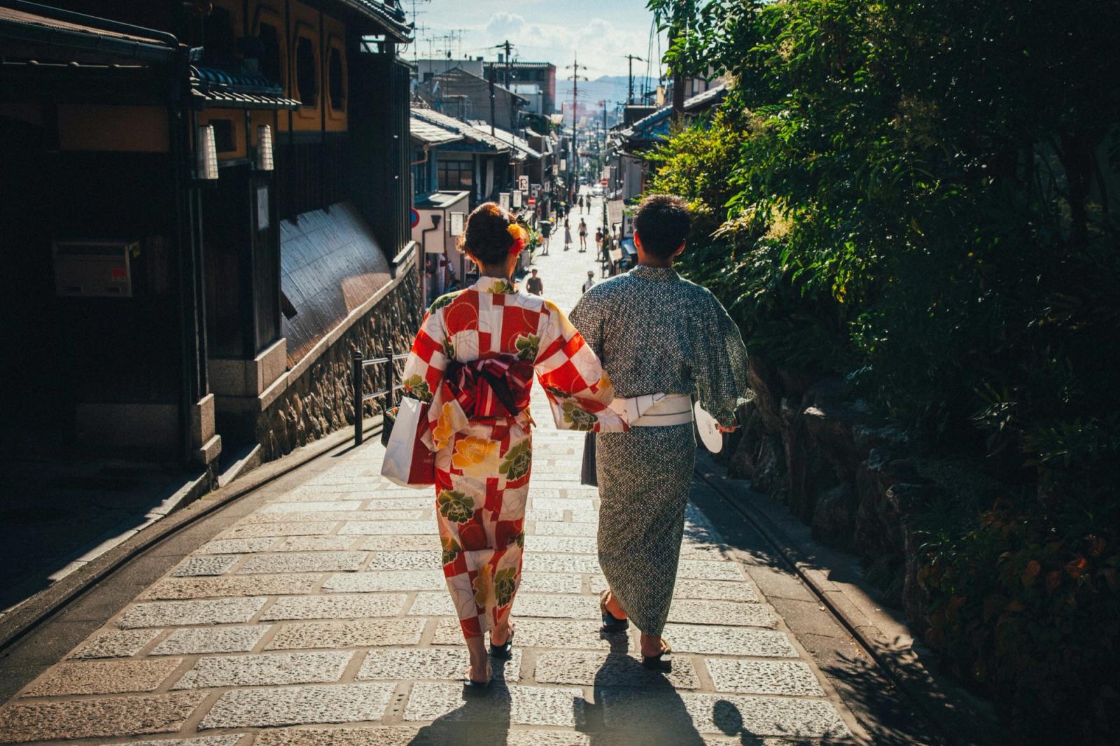 Una pareja en yukata baja del brazo por una calle empedrada de Kioto, a contraluz