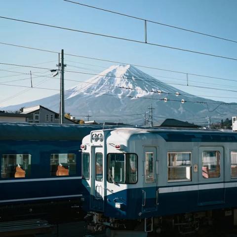 El monte Fuji nevado detrás de un tren local azul, con cielo despejado