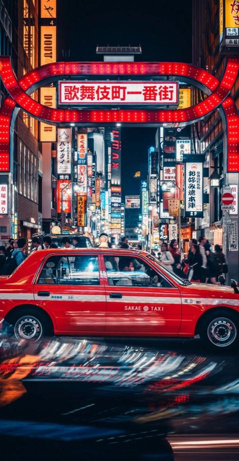 Un taxi rojo pasa bajo el arco luminoso de Kabukicho, en Shinjuku, de noche