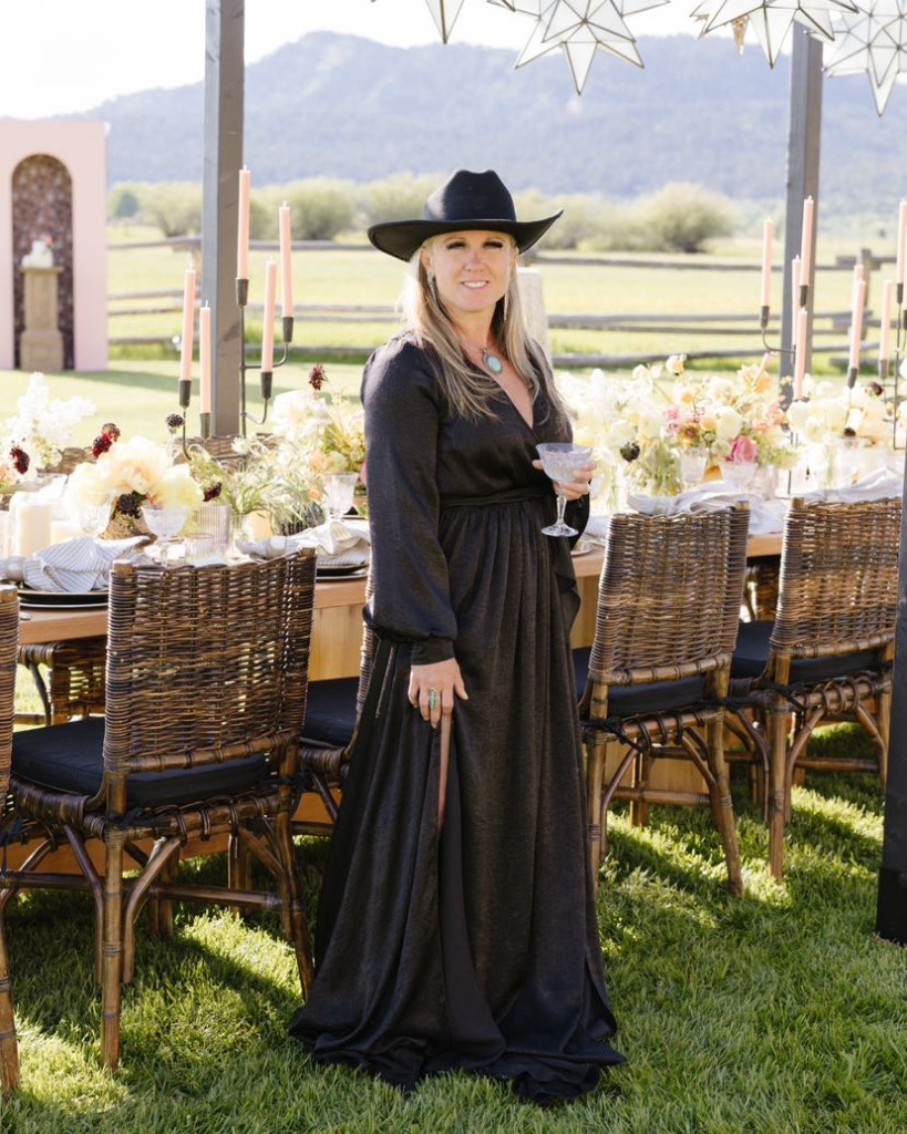 Kindryn in a black dress and cowboy hat beside an outdoor banquet table of flowers