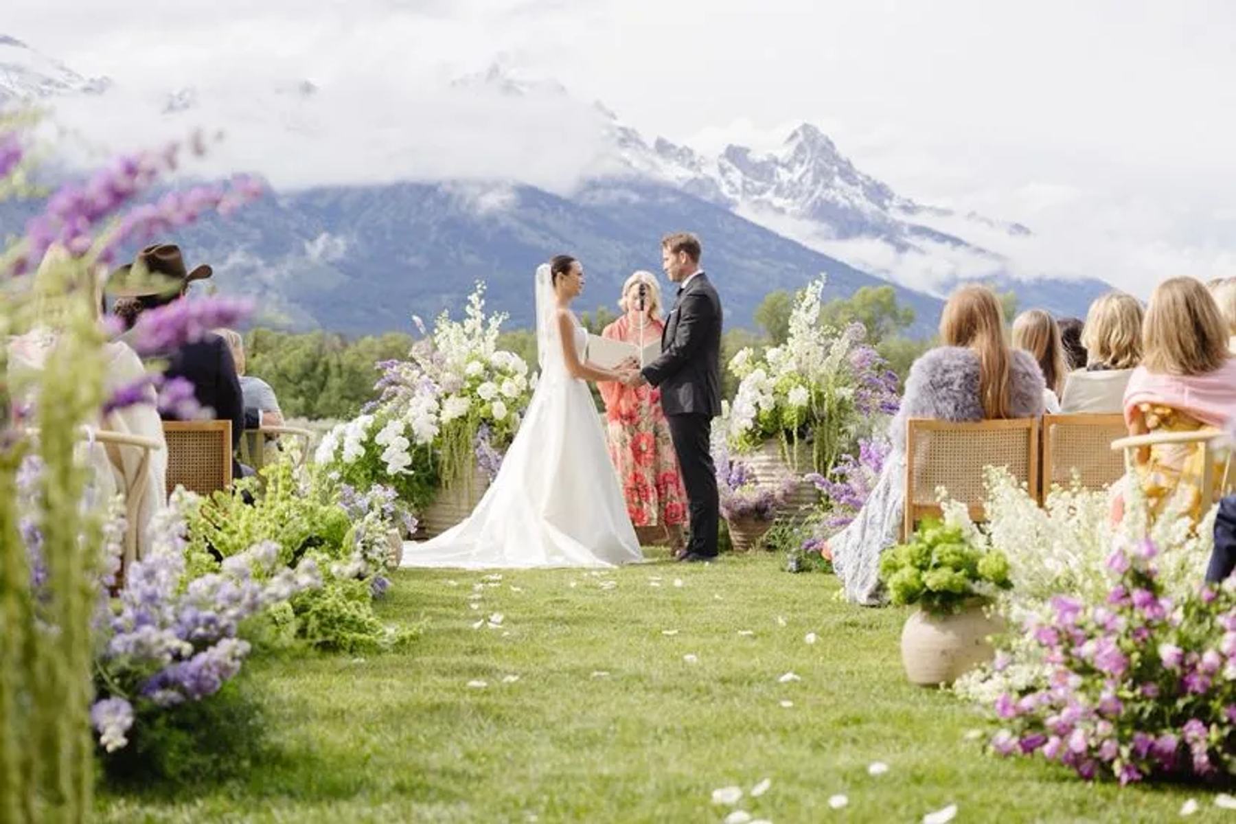 A mountain wedding ceremony with lavender ground florals and the Tetons behind the couple