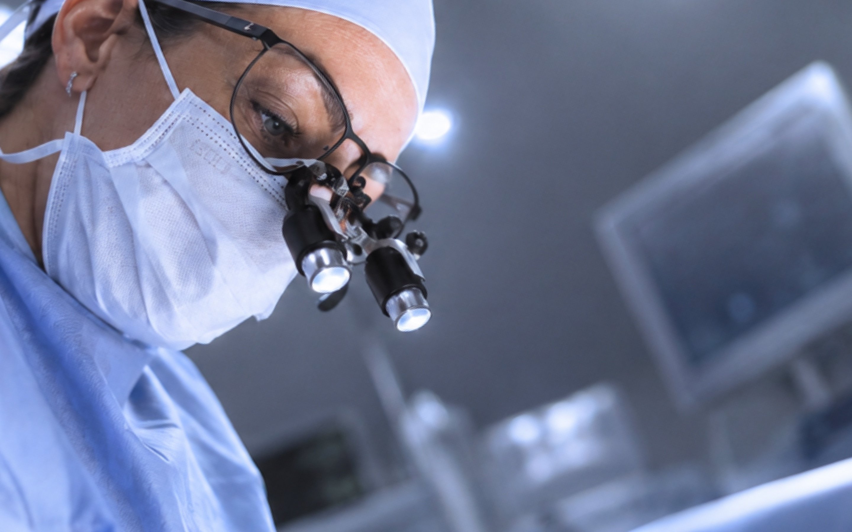 Un chirurgien masqué, équipé de loupes binoculaires, concentré pendant une opération.