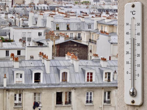 Thermomètre accroché à une façade, devant des toits d’immeubles parisiens