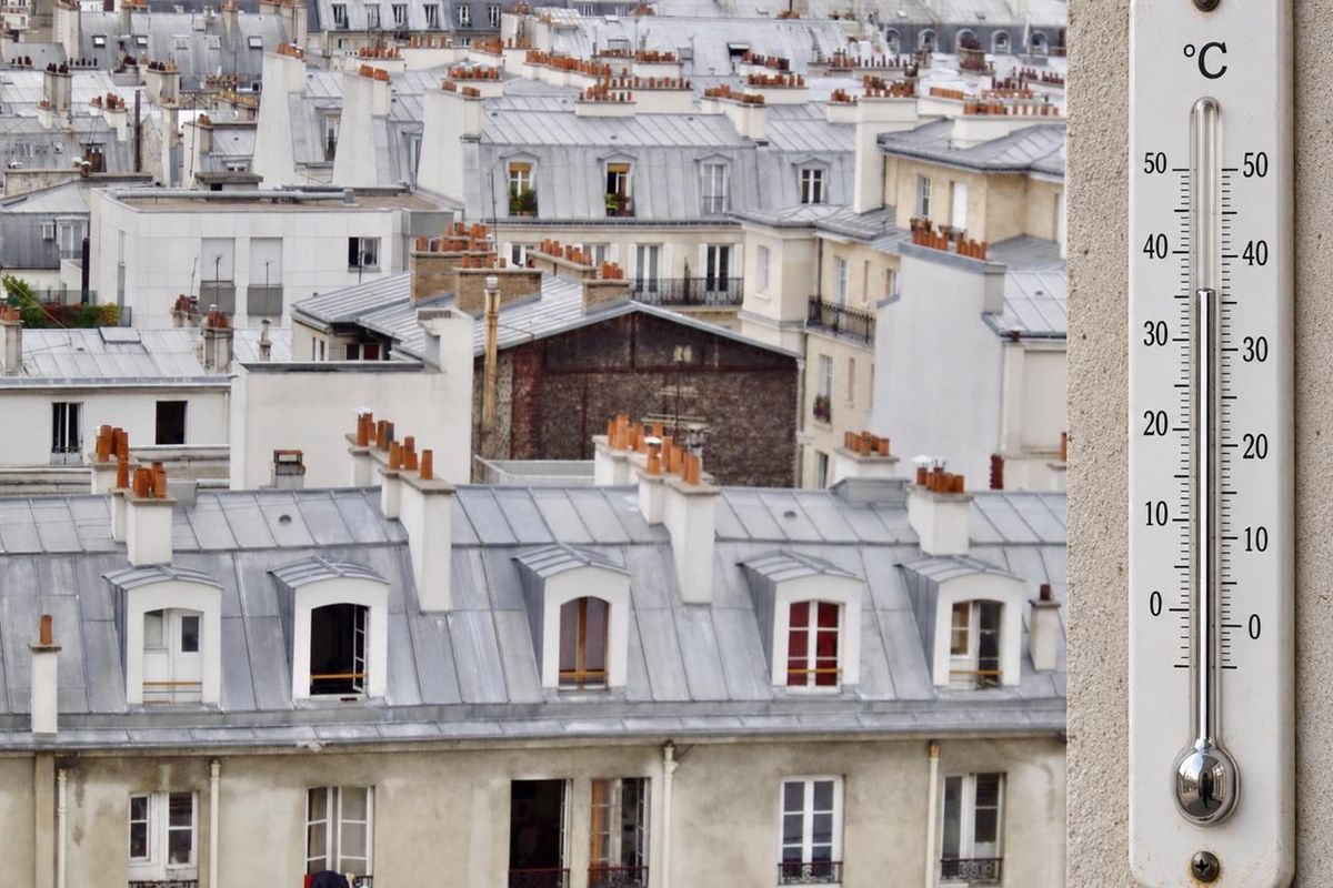 Thermomètre accroché à une façade, devant des toits d’immeubles parisiens