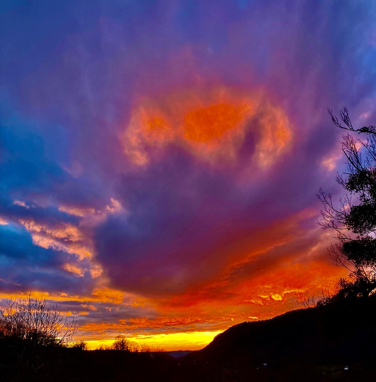 Ciel embrasé de rouge et de violet au coucher du soleil, au-dessus de collines boisées