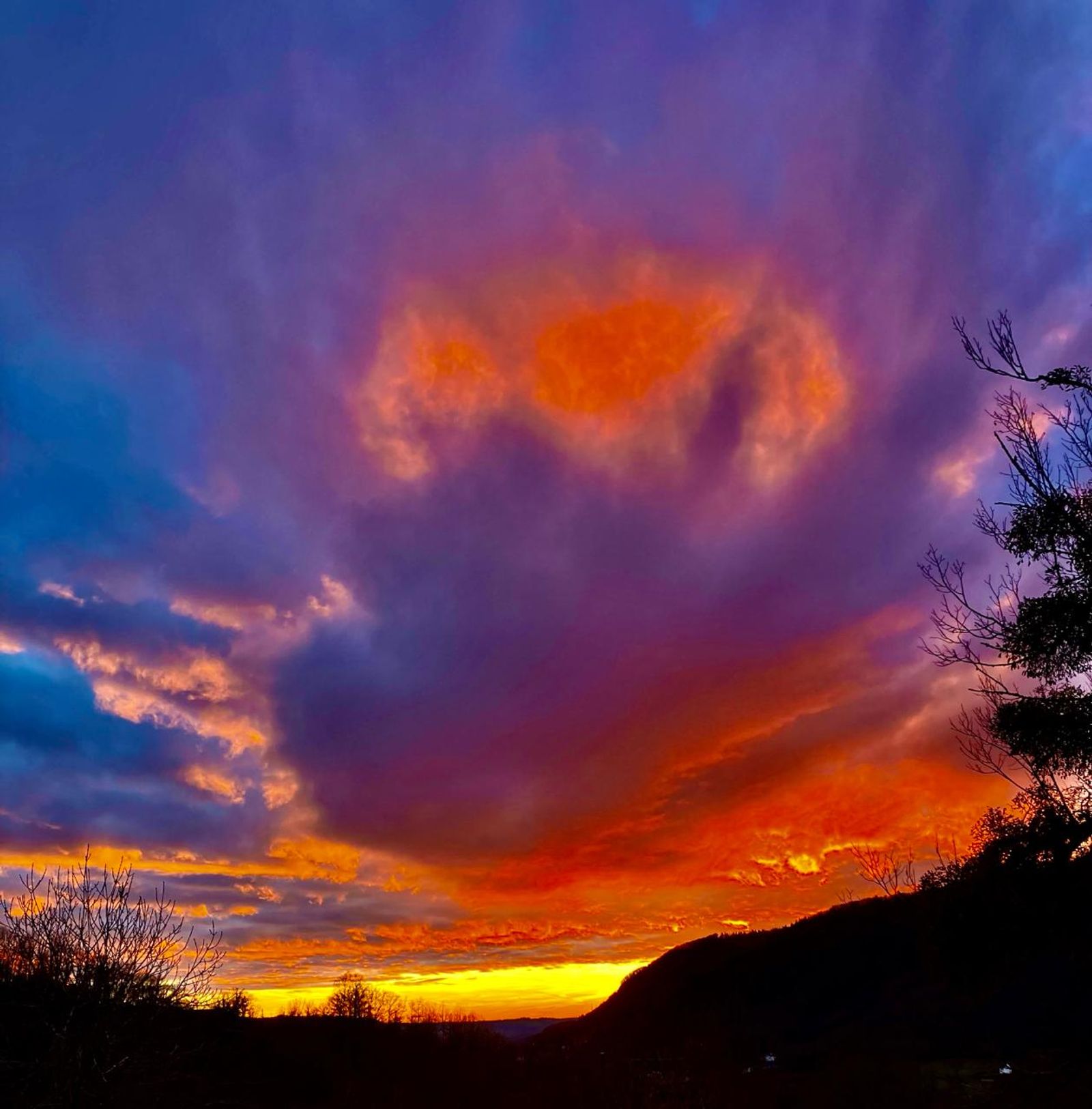 Ciel embrasé de rouge et de violet au coucher du soleil, au-dessus de collines boisées