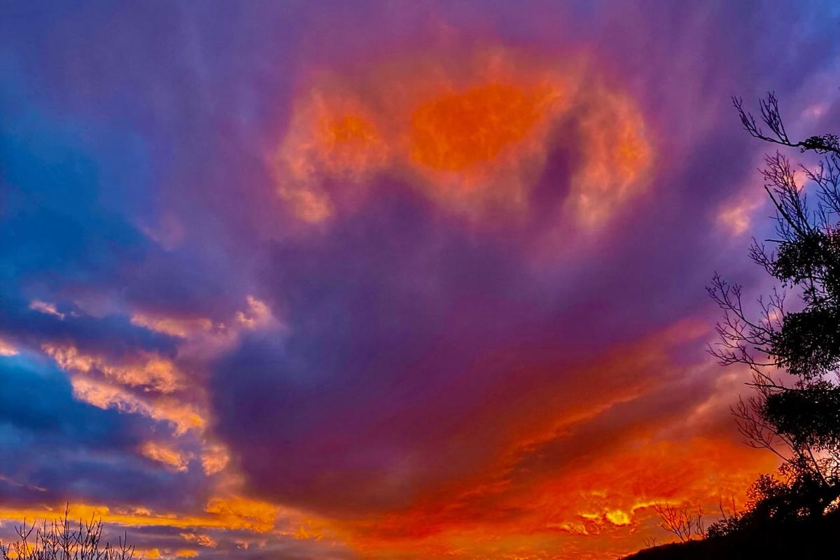 Ciel embrasé de rouge et de violet au coucher du soleil, au-dessus de collines boisées