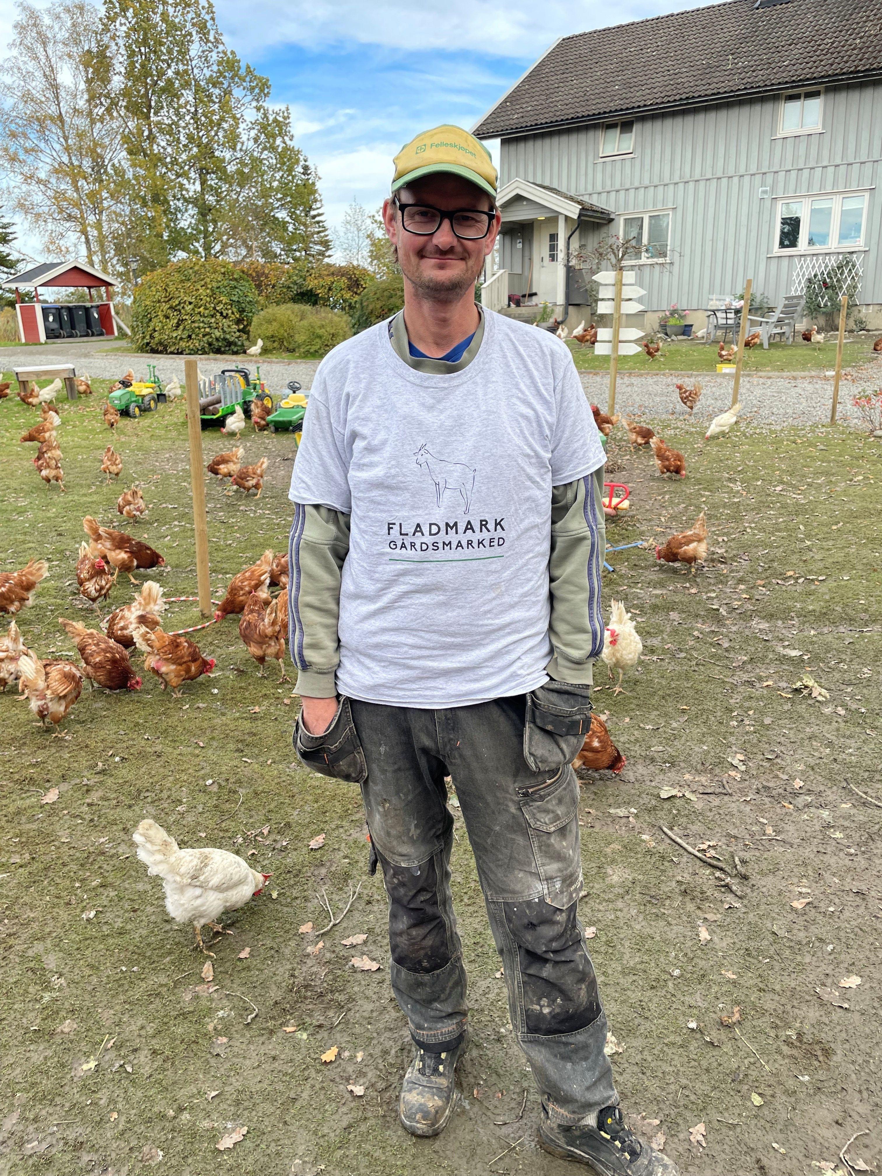 Mann som står blant mange høner