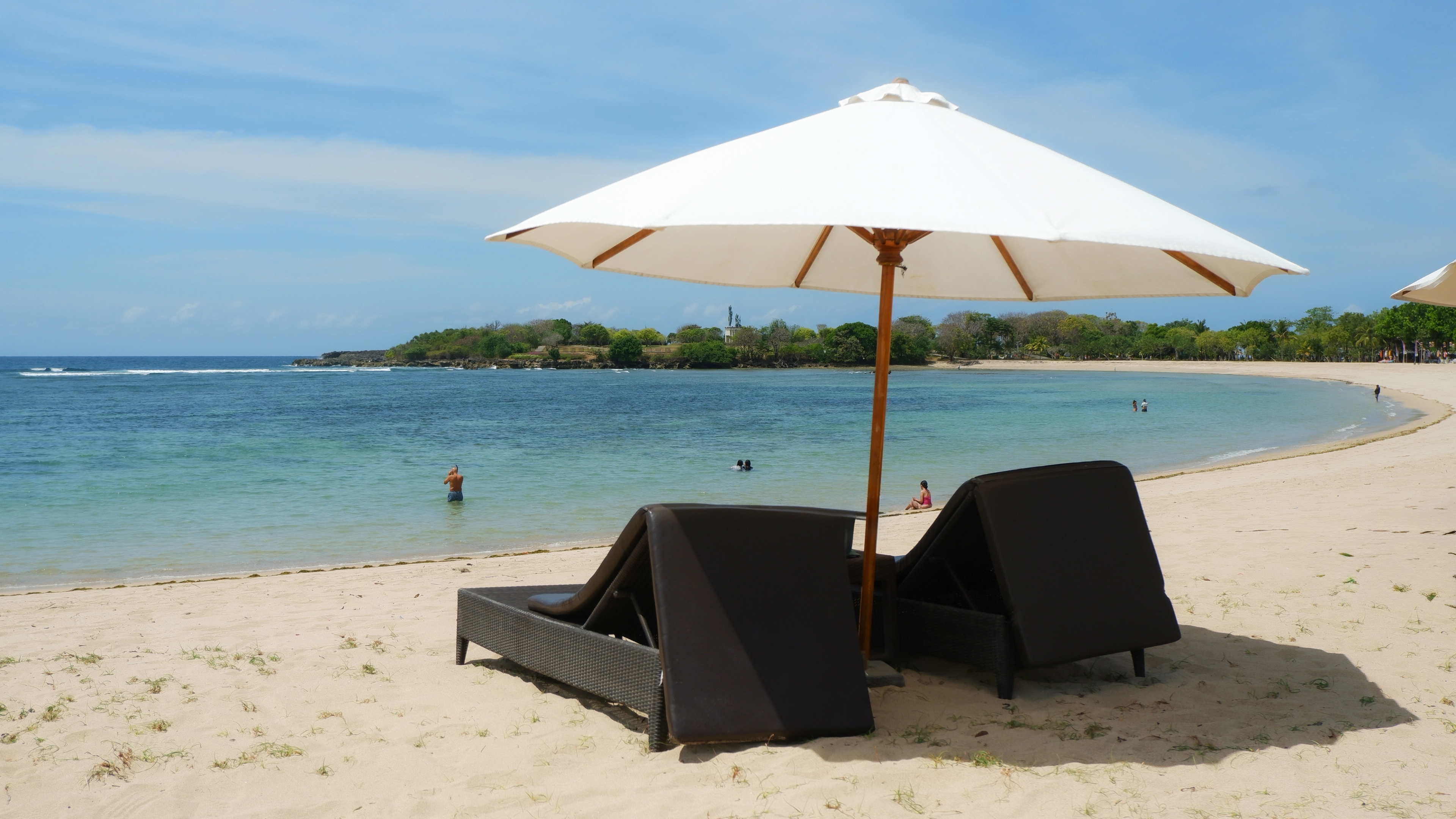 Image of two sunbedsand umbrella on the beach in Nusa Dua, in the ocean people are swimming