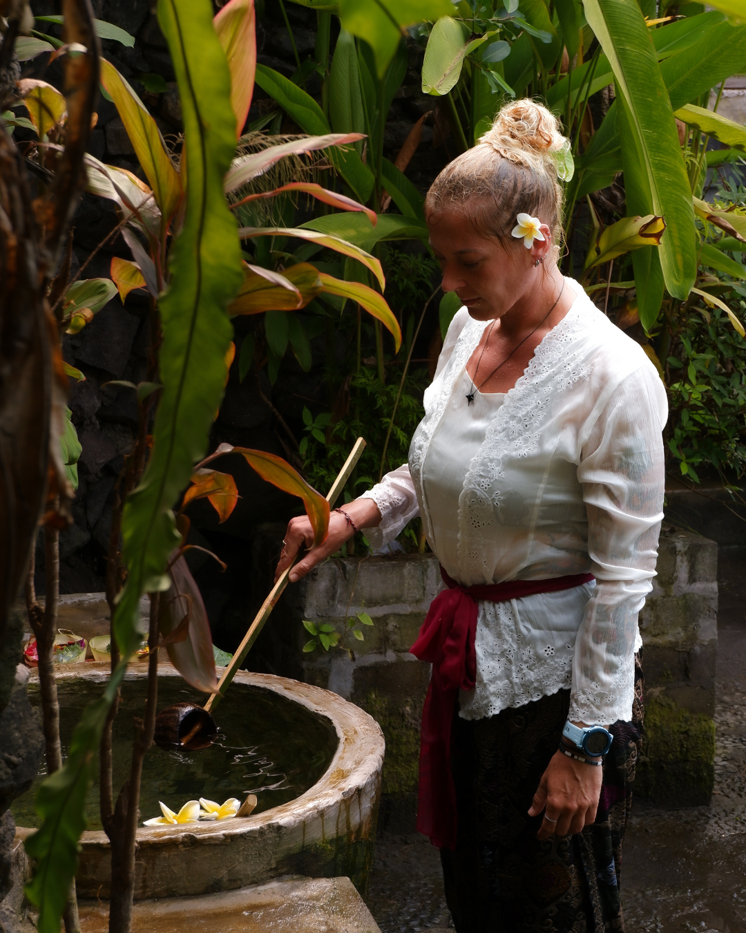 Image shows woman in temple during melukat ceremony, she wears sarong around the waist, a sash tied firmly at the waist, shoulders covered, bare feet within temple grounds
