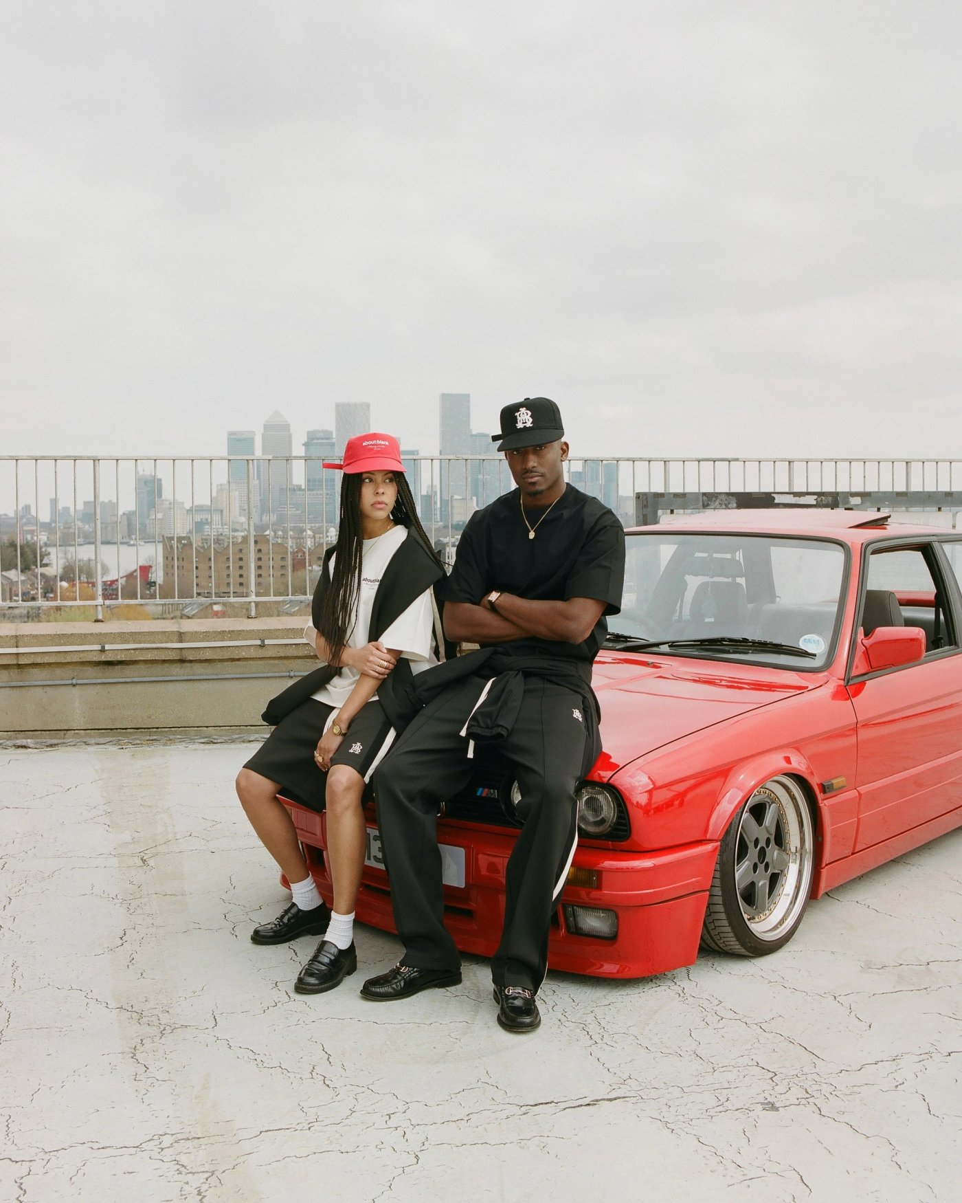 Two people leaning on a red BMW 3 Series on a London rooftop