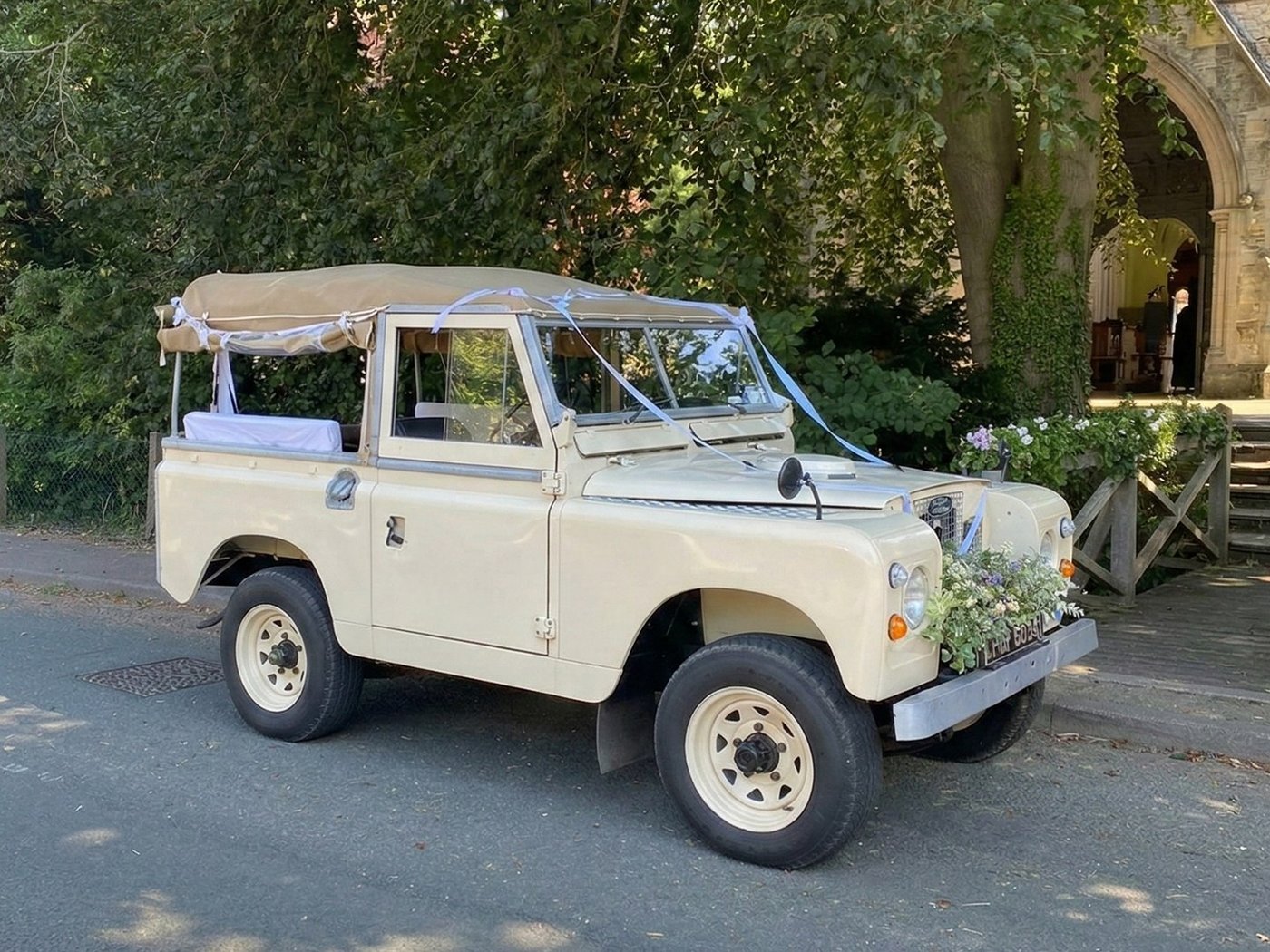 A cream Land Rover Series 2 dressed with ribbons outside a church