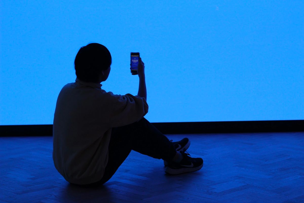 Person silhouetted against a uniform blue colour field holding up their mobile phone as if recording a video