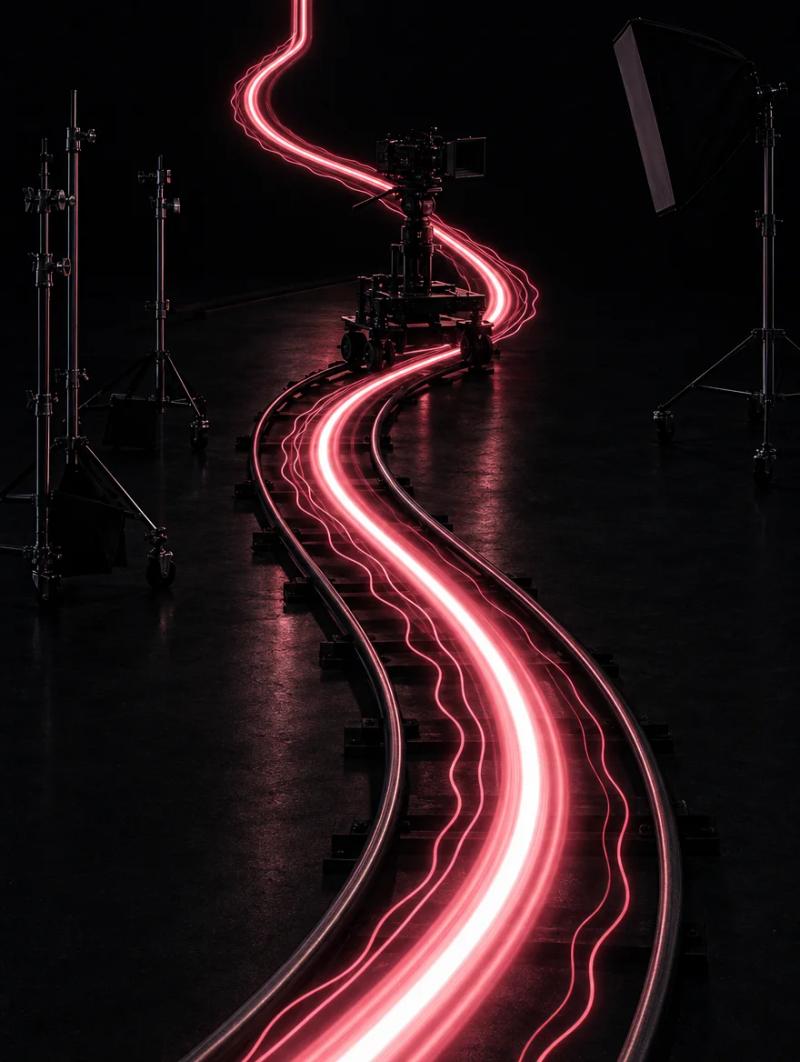 Fotografia a lunga esposizione: scie di luce rosa seguono il binario di un carrello da ripresa in uno studio buio.