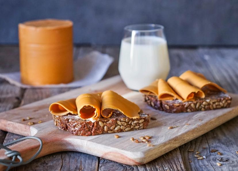 a wooden cutting board topped with slices of cheese and a glass of milk .