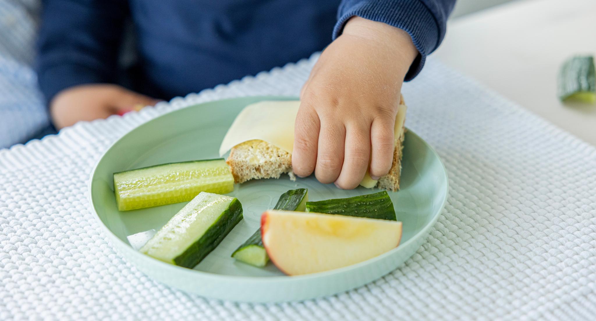a child is eating a sandwich and vegetables on a plate .