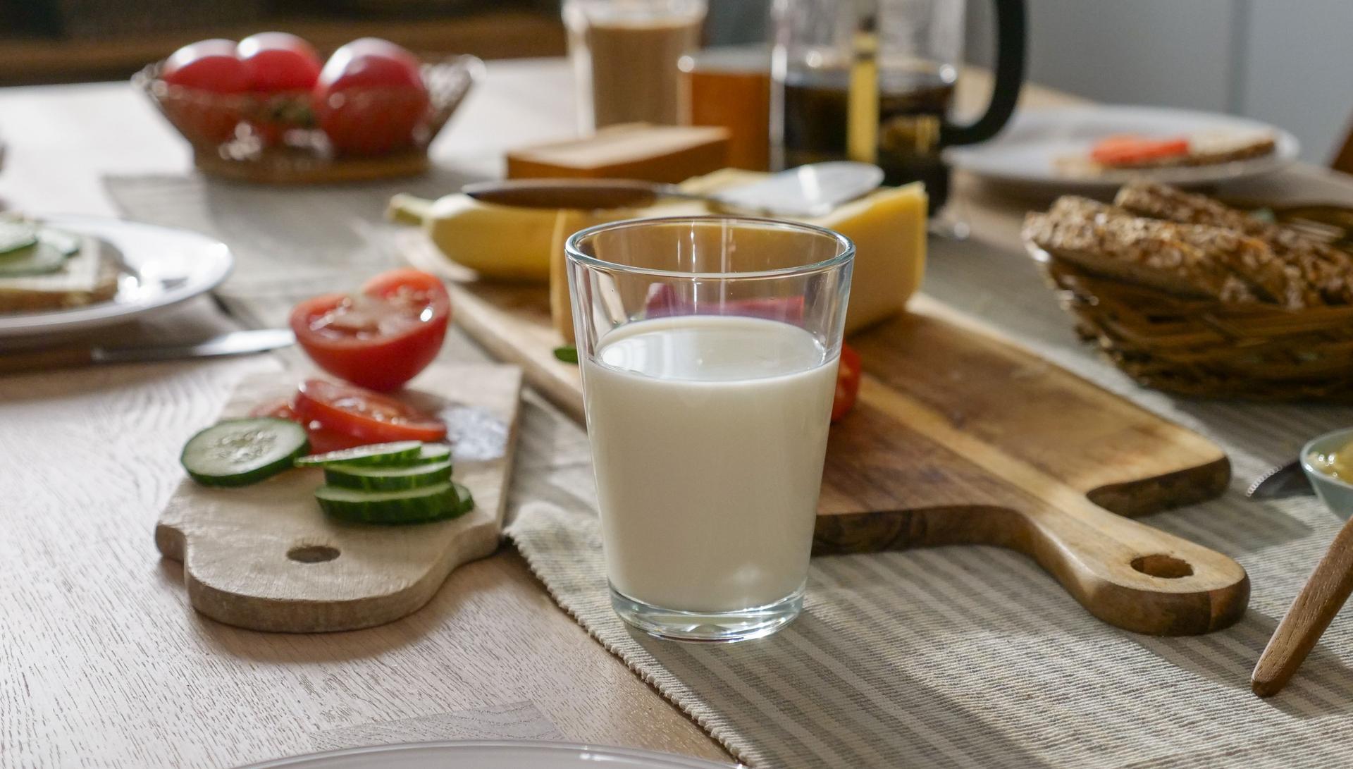 Frokostbord med melk, skjærebrett med agurk og tomat på, grovbrød, hvitost og brunost.