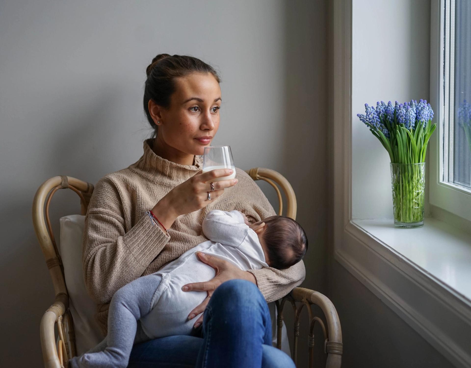 a woman is holding a baby and drinking a glass of milk .