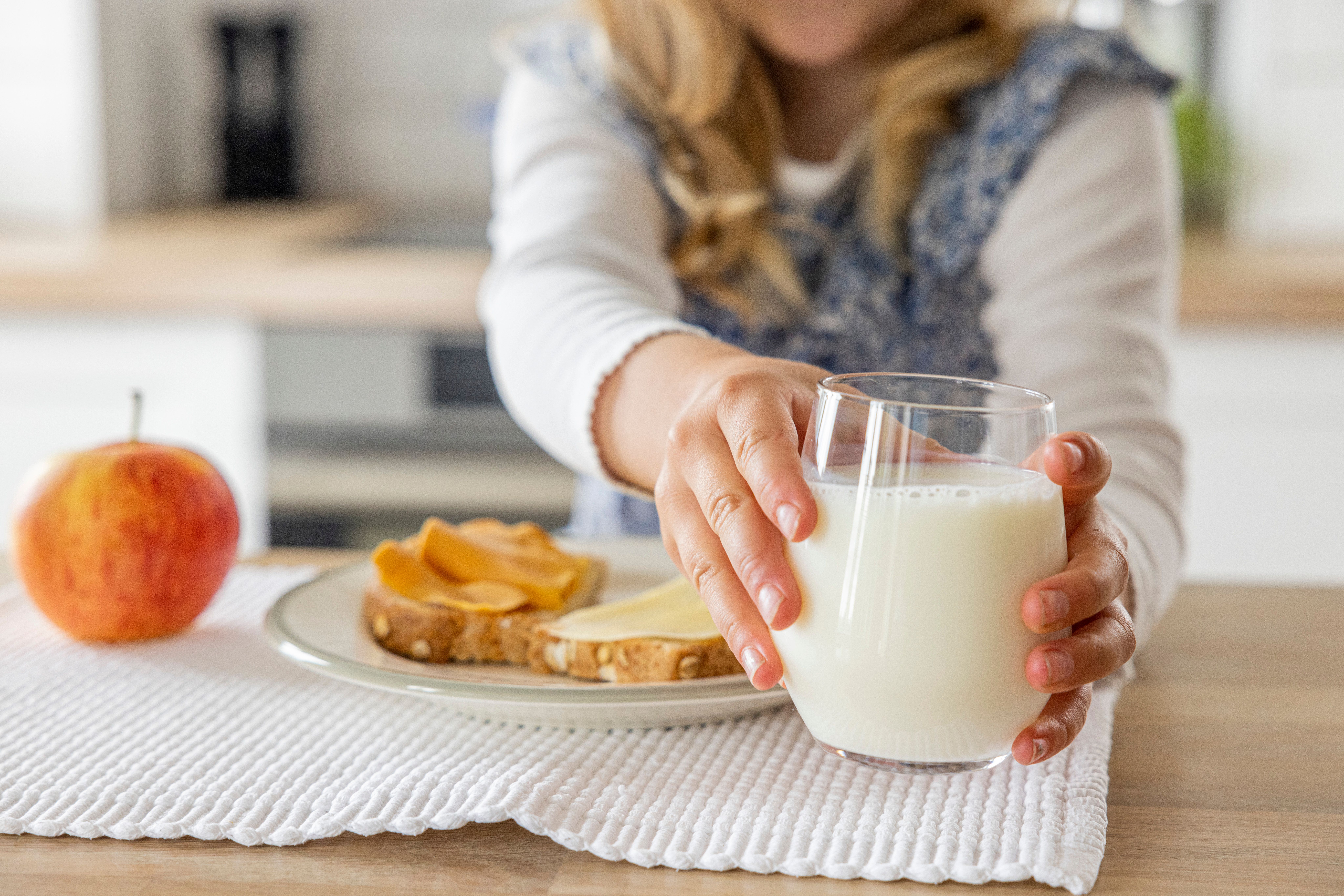 Child reaching for a glass of milk, with toast and an apple on the table.