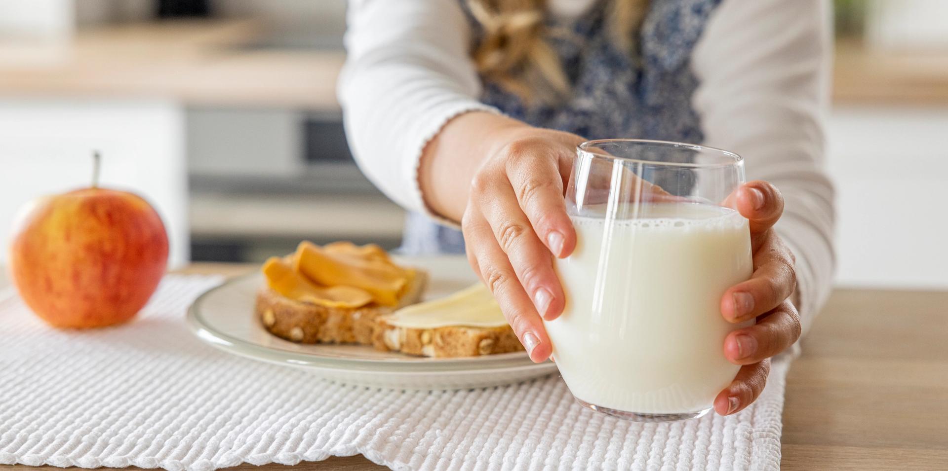 Child reaching for a glass of milk, with toast and an apple on the table.